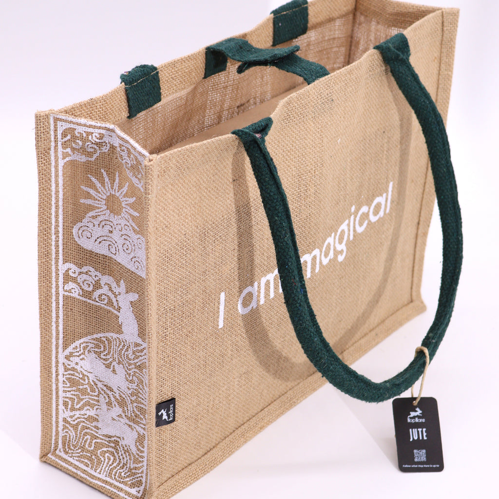 A beige jute bag, with green handles, with the text 'I am magical' printed on the side, featuring a moon and hare design.