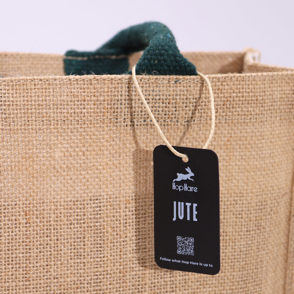 A close up of a beige jute bag, with green handles and a black HopHare tag.