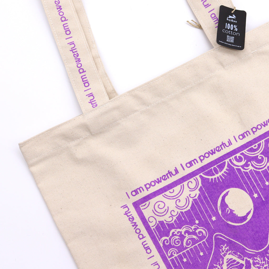 Tote bag with purple motif which is of wolves howling to the moon with the affirmation "I am powerful" repeated around the motif. 