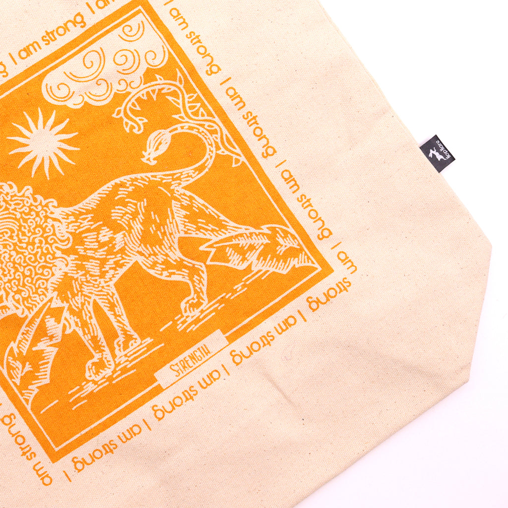 Tote bag with yellow motif which is of a lion with the affirmation "I am strong" repeated around the motif. 