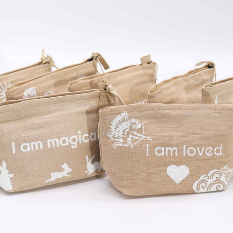 A collection of beige jute pouches with various affirmations printed on them, such as 'I am magical' and 'I am loved'.