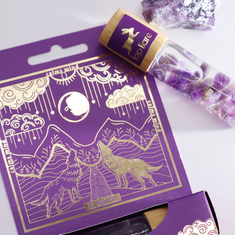 A purple roll-on essential oil bottle with a gold-printed tarot card, set against a packaging with a wolf illustration.