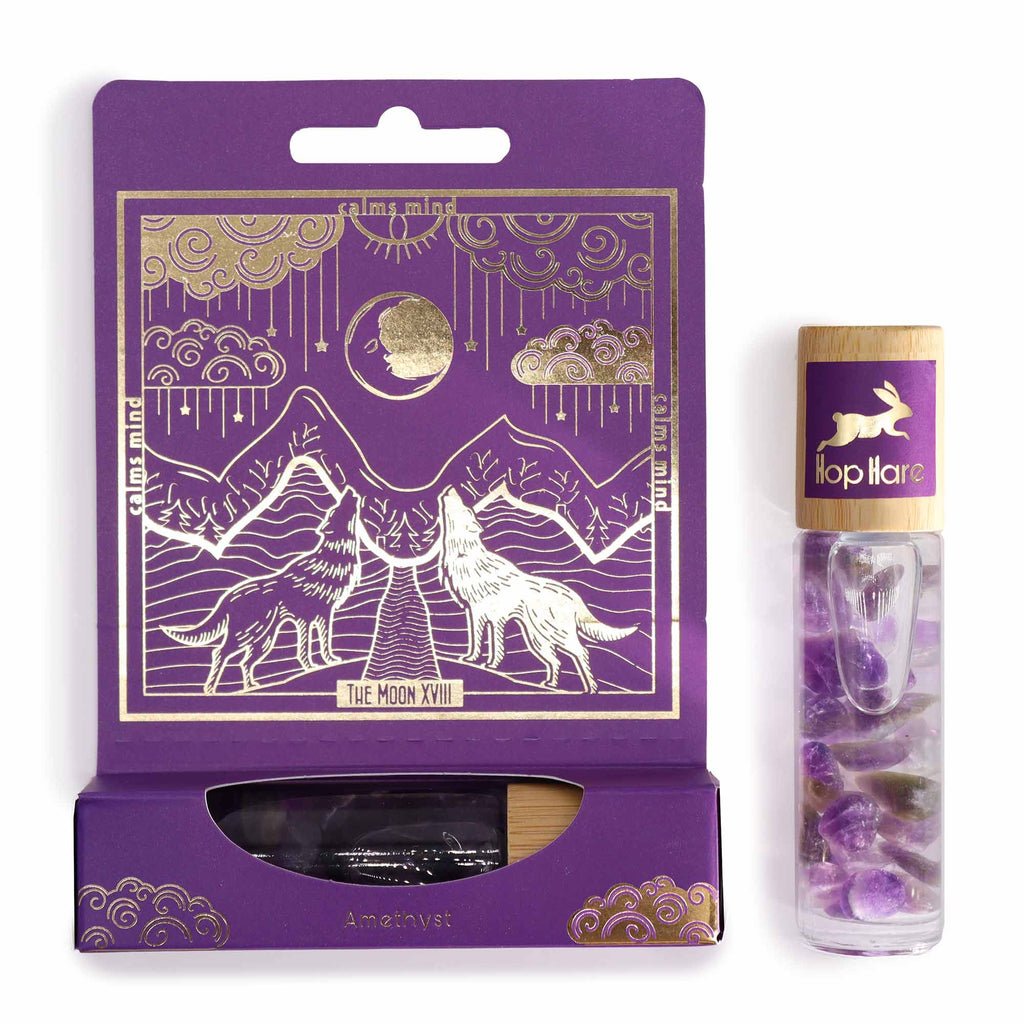 A purple roll-on essential oil bottle with a gold-printed tarot card, set against a packaging with a wolf illustration.
