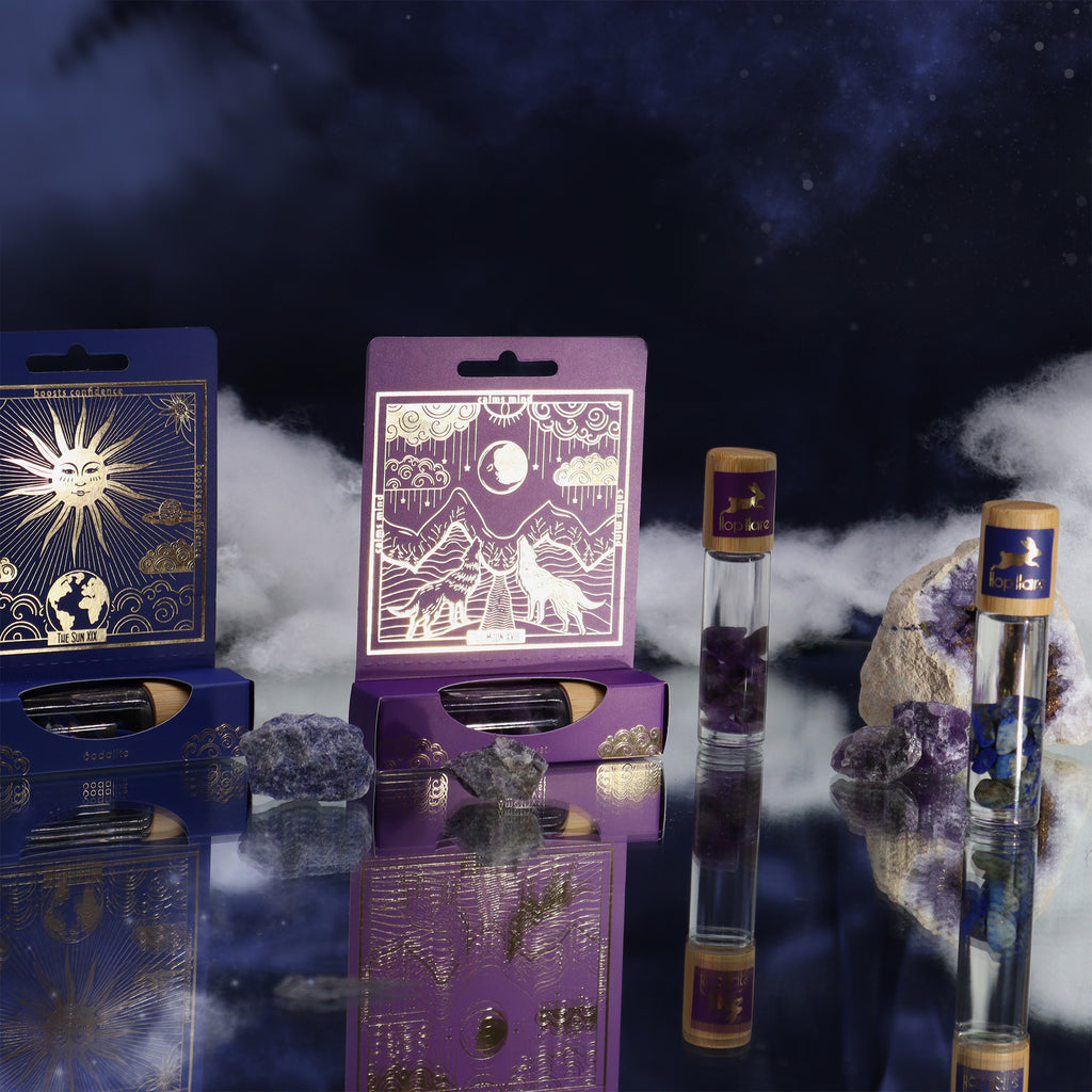 A purple roll-on essential oil bottle with a gold-printed tarot card, set against a packaging with a wolf illustration alongside a blue theme "Sun" one.