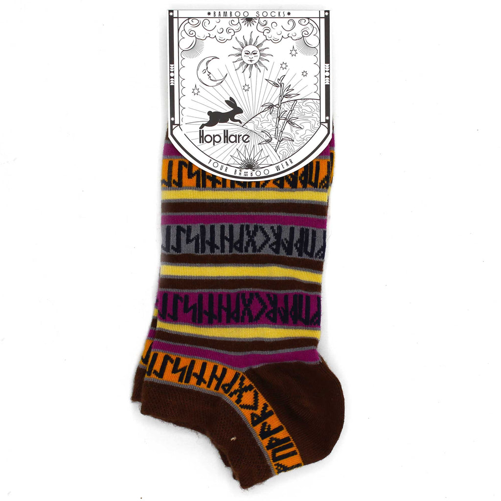 A pair of ankle socks which are brown, with stripes of orange, pink, grey and cream with black runes, on a white surface - tied together with a card tag with a HopHare design 