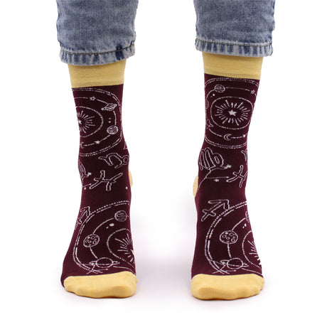 A pair of maroon bamboo socks with white Zodiac patterns and yellow cuffs, worn with blue jeans.
