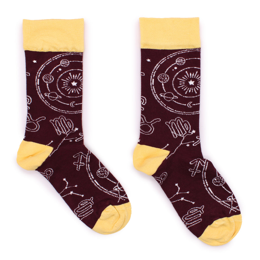 A pair of maroon bamboo socks with white Zodiac patterns and yellow cuffs, laid on a white surface 