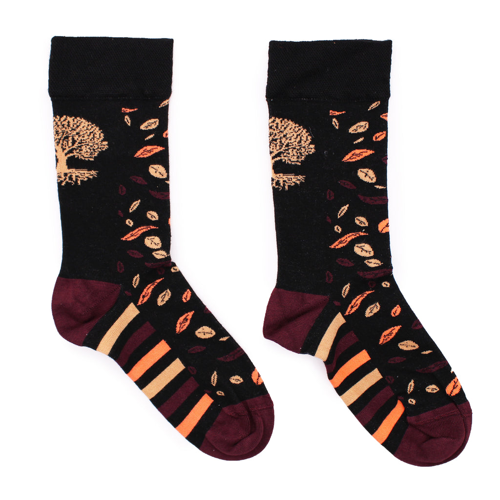 A pair of mostly black bamboo socks with a gold tree of life symbol design, with maroon, cream and pale orange stripes across the bottom and the same coloured leaves across the top, laid on a white background.
