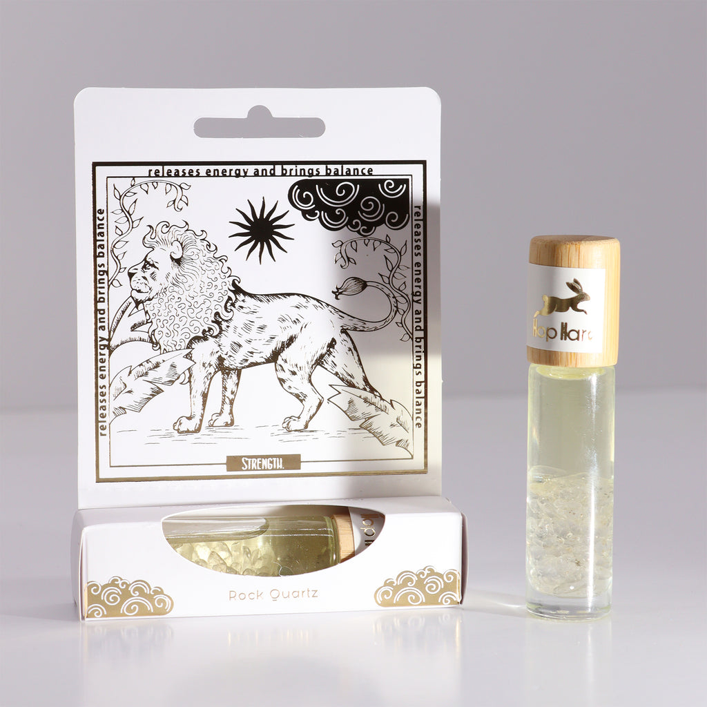 An essential oil gemstone roll-on bottle with a gold-printed tarot card, alongside its packaging. The roll-on bottle is clear, and the packaging features a line art design with a lion and a sun.