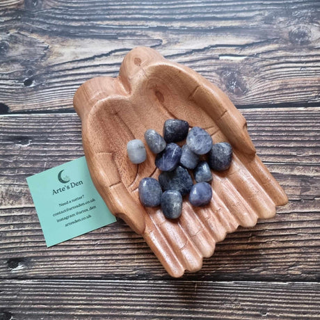 A collection of Iolite Tumblestones displayed in a wooden hand-shaped dish with a business card beside it, on a wooden background.