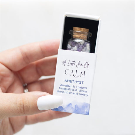 A hand holding a white matchbox-style gift box labelled 'A Little Jar of Calm' with a small glass jar filled with purple amethyst crystal chips inside.
