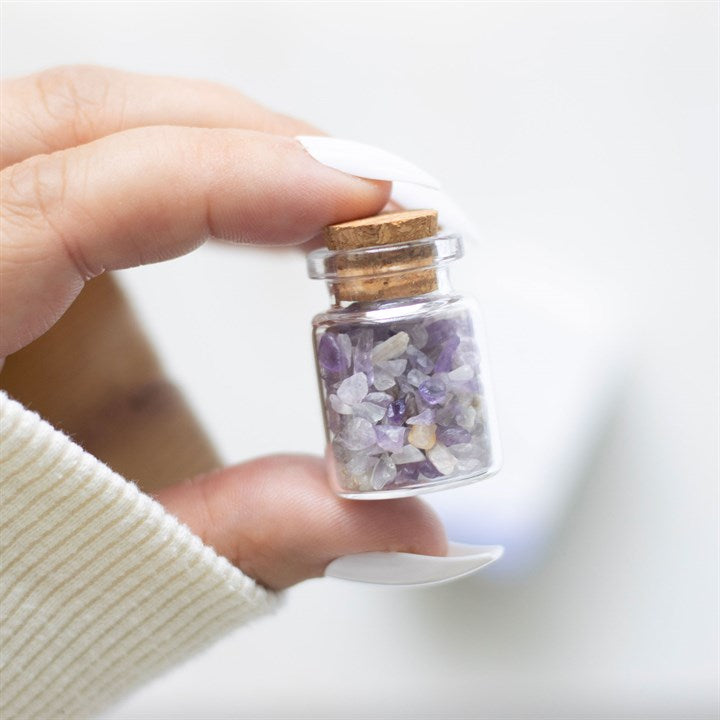 A hand holding 'A Little Jar of Calm' with a small glass jar filled with purple amethyst crystal chips inside.