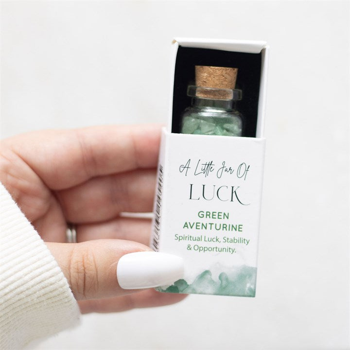 A hand holding a white matchbox-style gift box labelled 'A Little Jar of Luck' with a small glass jar filled with green aventurine crystal chips inside.