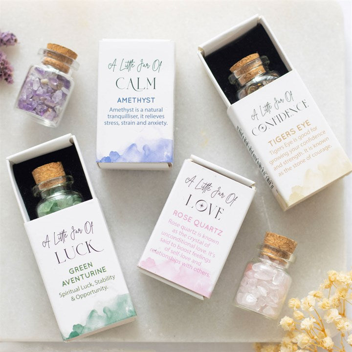 A collection of white matchbox-style gift boxes labelled 'A Little Jar of...'  with a small glass jar filled with crystal chips inside.