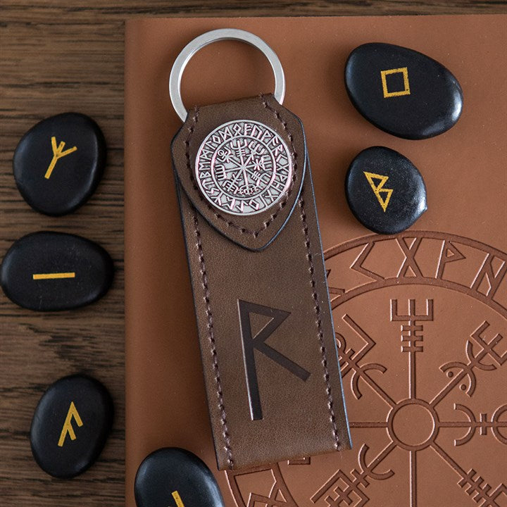 Faux brown leather keychain with silver emblem and runes, surrounded by black stones with symbols on a brown surface.