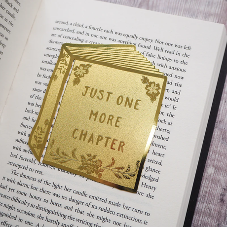 Brass bookmark with 'Just One More Chapter' text on an open book