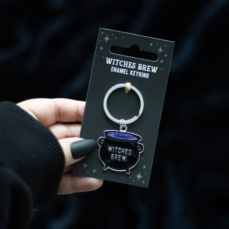 A hand holding a cauldron key ring which says "Witches Brew" on a black card. 
