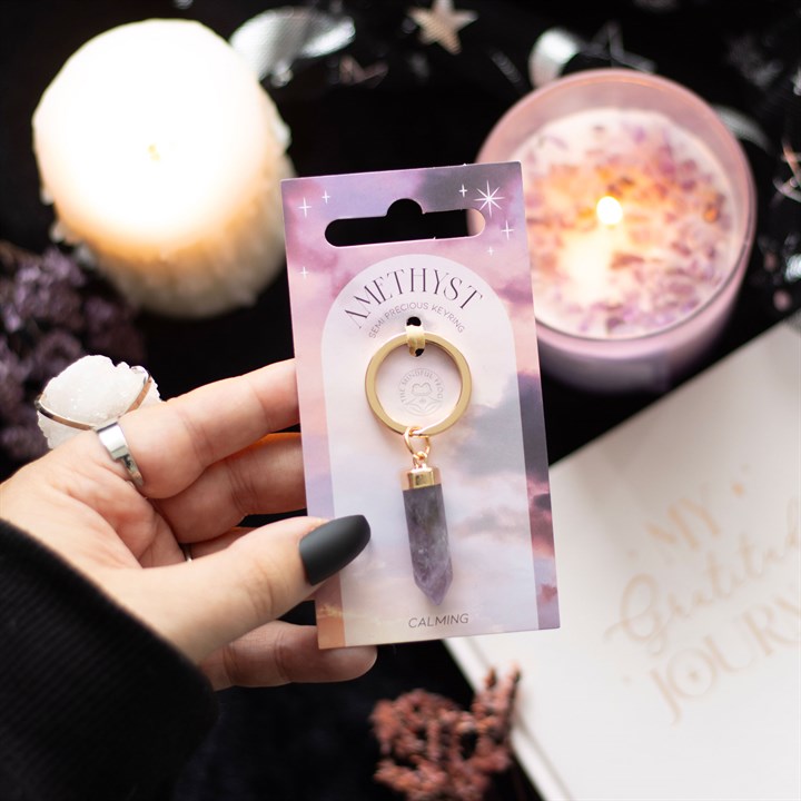 A hand holding an Amethyst crystal key rings on display and gold-coloured keyring attachment, presented on pink and purple backing cards with a star pattern.