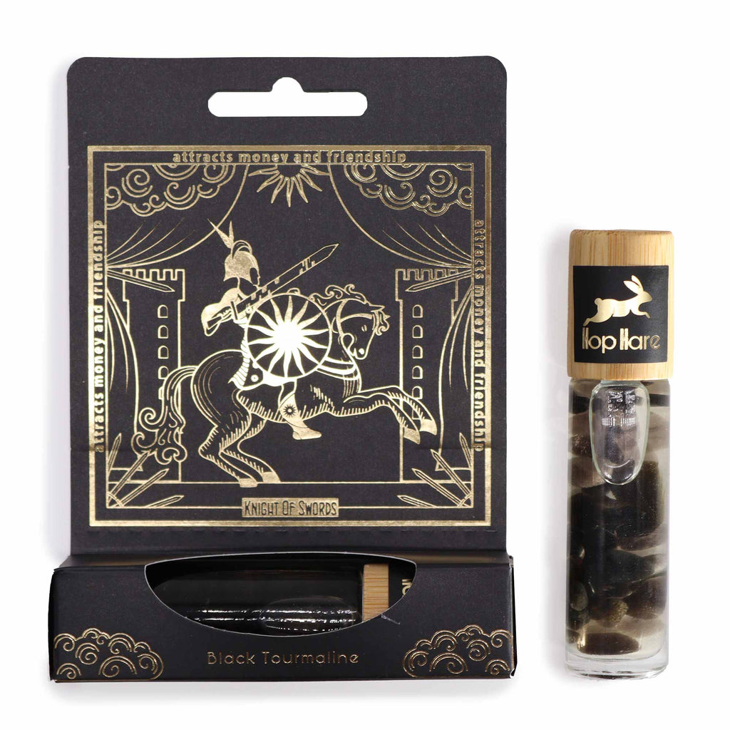 An essential oil gemstone roll-on with a wooden cap, labelled 'The Knight of Swords' by Hop Hare, accompanied by black tarot cards with gold illustrations.
