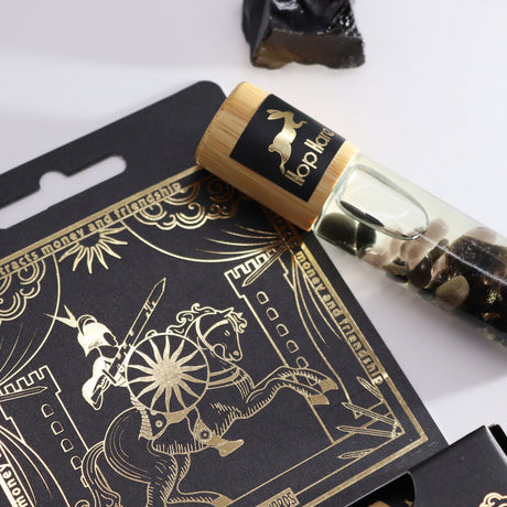 An essential oil gemstone roll-on with a wooden cap, labelled 'The Knight of Swords' by Hop Hare, accompanied by black tarot cards with gold illustrations.