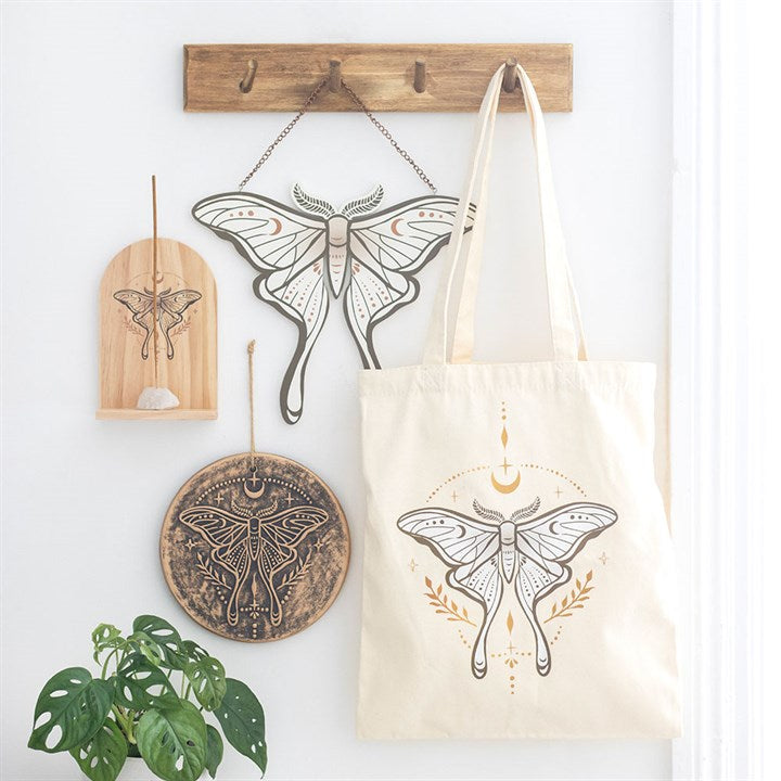 A lunar moth cotton tote bag hung up on a wooden hanger with other lunar moth decorations 