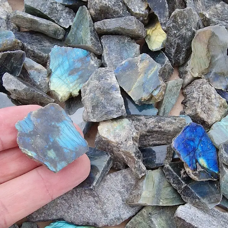 Hand holding a labradorite gemstone amidst a pile of similar stones