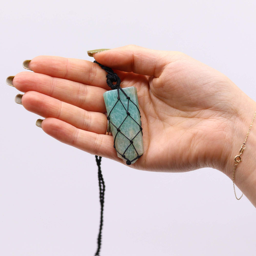 A flat point pendant with am Amazonite gemstone, laced into a black necklace with an adjustable string, held in a hand
