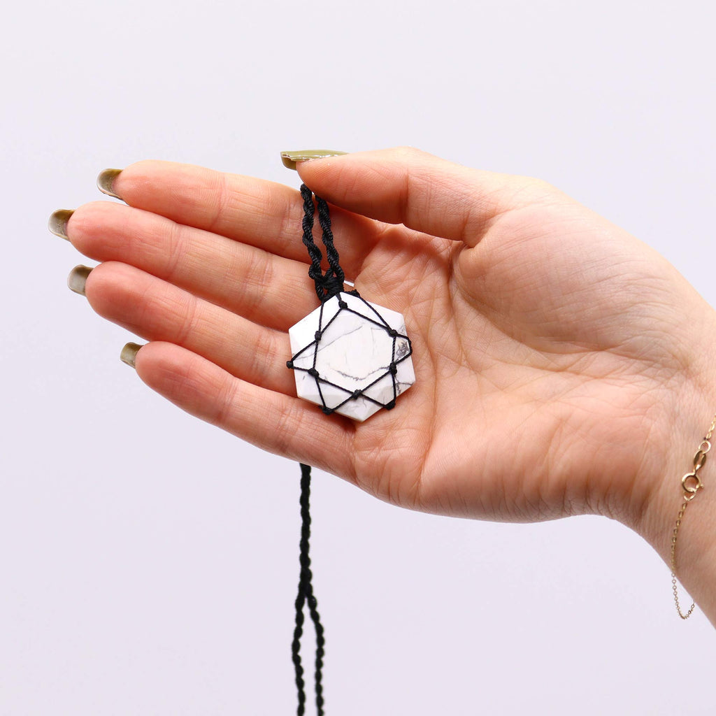 A hexagon pendant with a White Howlite gemstone, laced into a black necklace with an adjustable string, held in a hand
