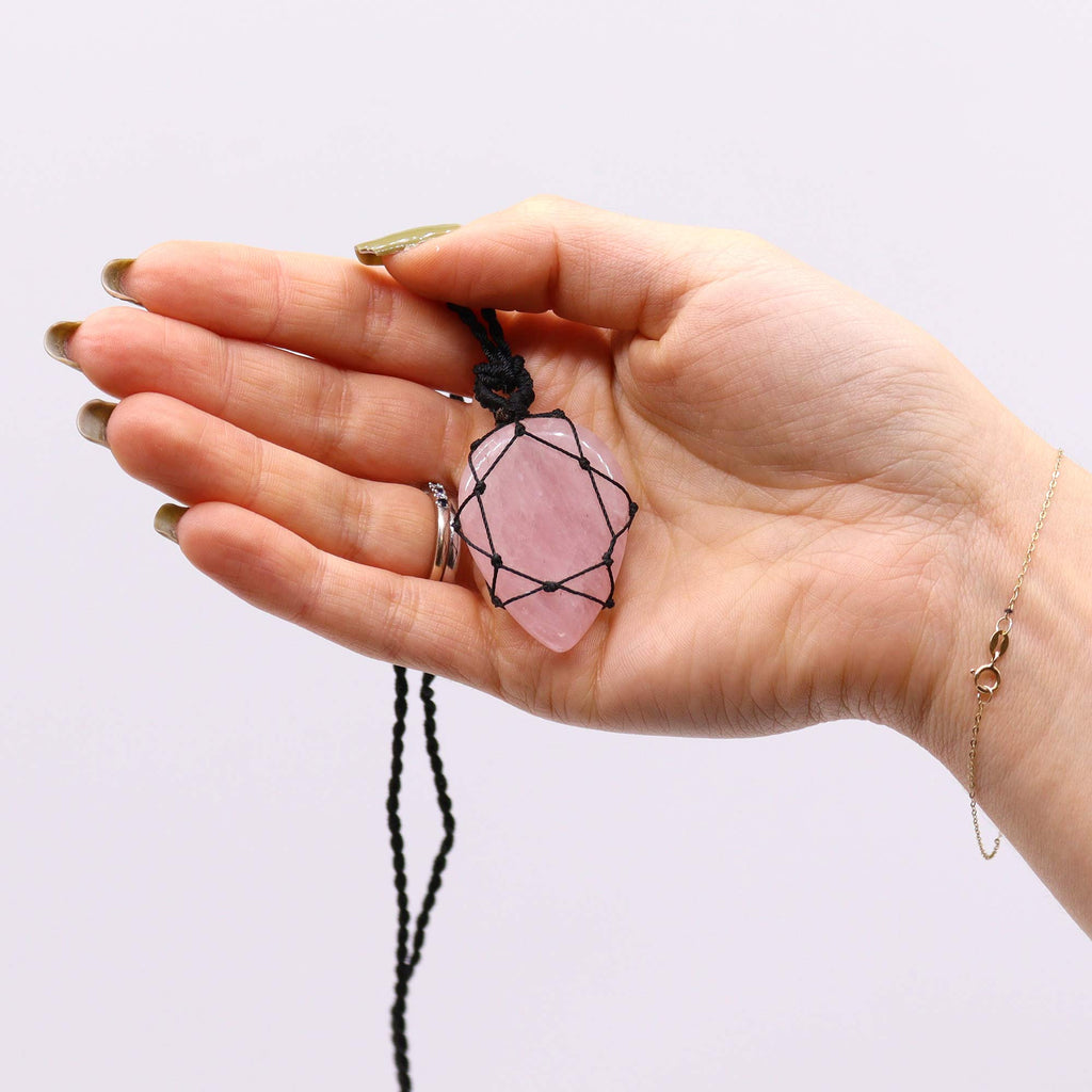 A teardrop shaped pendant with a Rose Quartz gemstone, laced into a black necklace with an adjustable string, held in a hand