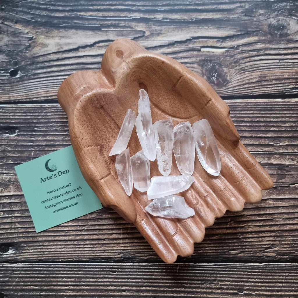 A collection of laser quartz points displayed in a wooden hand-shaped dish with a business card beside it, on a wooden background.