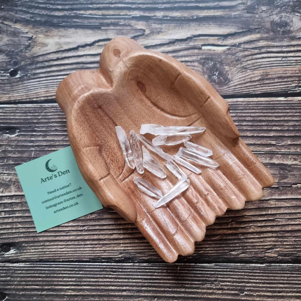 A collection of laser quartz points displayed in a wooden hand-shaped dish with a business card beside it, on a wooden background.