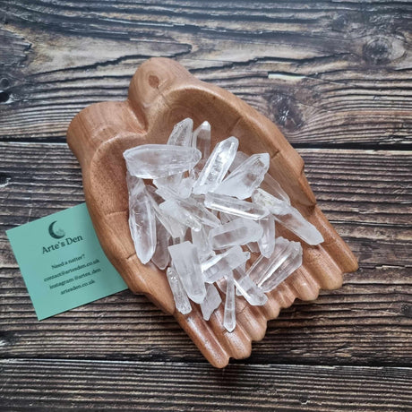 A collection of laser quartz points displayed in a wooden hand-shaped dish with a business card beside it, on a wooden background.