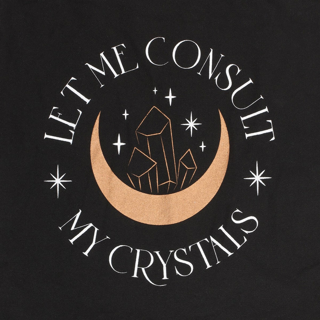 A close up of a black tote bag with crescent moon and crystal design which reads "Let me consult my crystals"