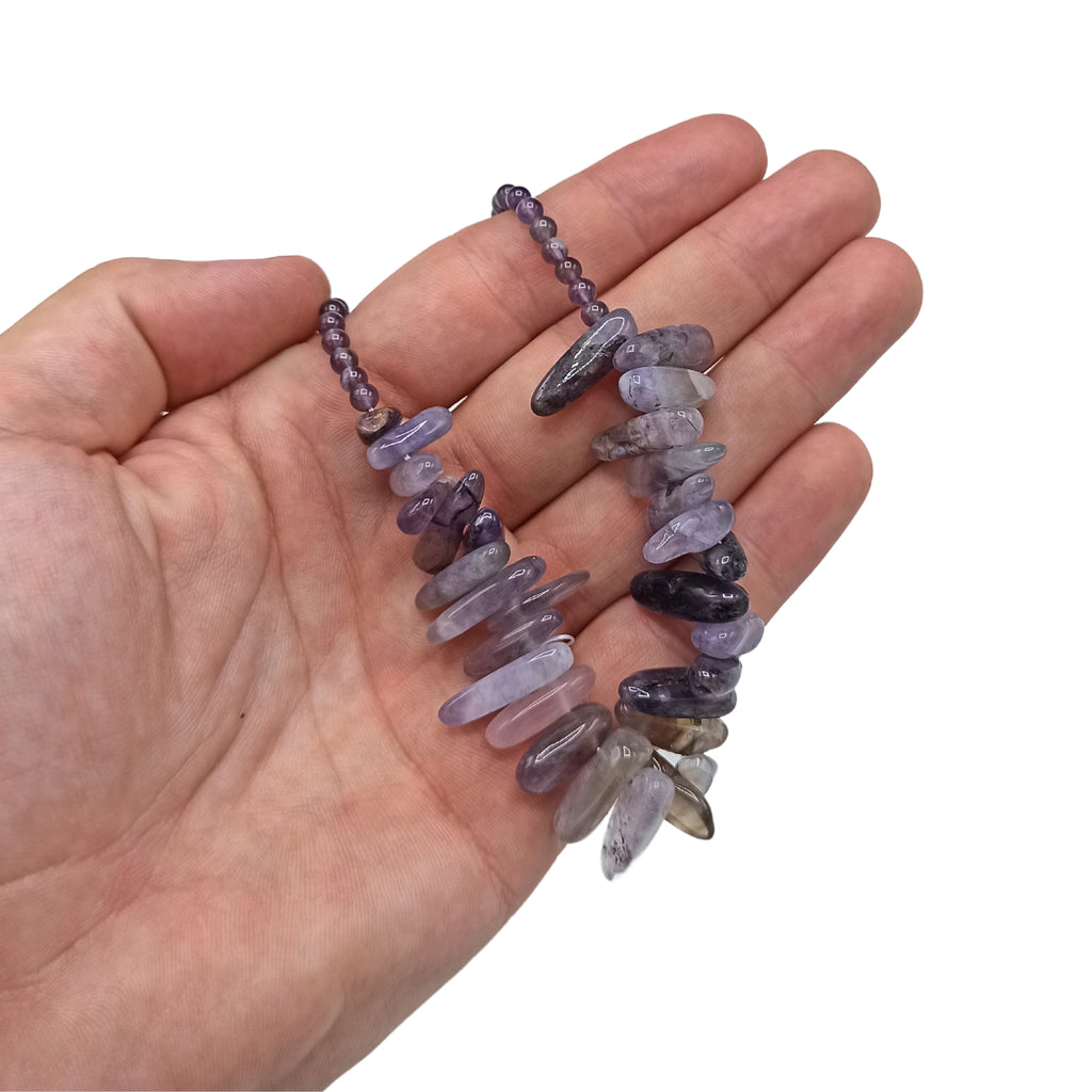 A purple longstone Amethyst necklace held in a hand.