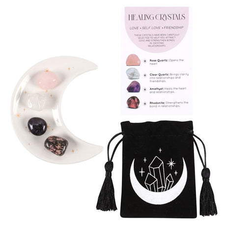 A set of healing crystals displayed with a crescent moon trinket dish, including a rose quartz, a clear quartz, amethyst and a rhodonite stone. The set is packaged in a black drawstring bag with a crescent moon design.