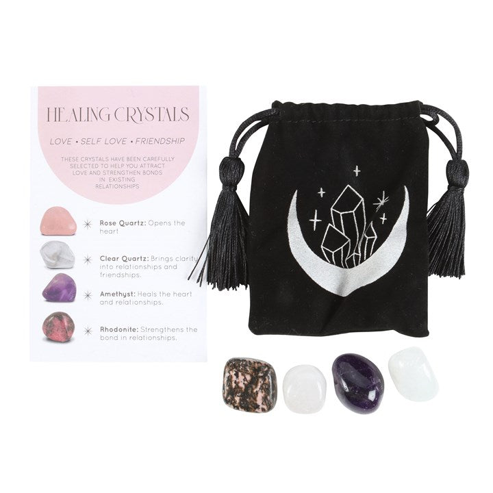 A set of healing crystals displayed with a crescent moon trinket dish, including a rose quartz, a clear quartz, amethyst and a rhodonite stone. The set is packaged in a black drawstring bag with a crescent moon design.