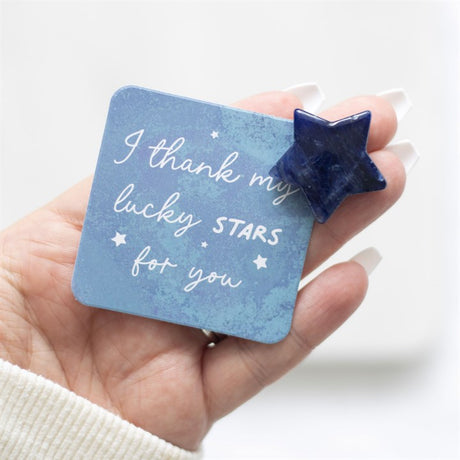 A hand holds a blue square card which reads "I thank my lucky stars for you" next to a blue crystal star