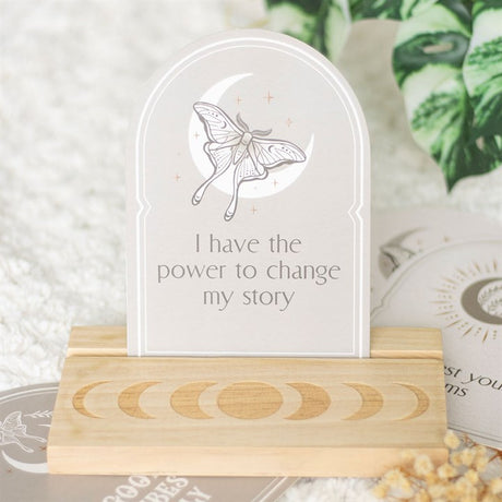 A beige affirmation card with a Luna moth design and the text 'I have the power to change my story' on it, placed on a wooden stand.