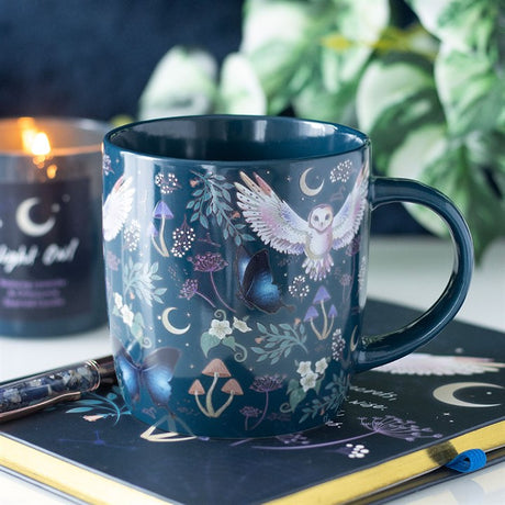 A blue mug with moths, owls, plants and moon deisgn
