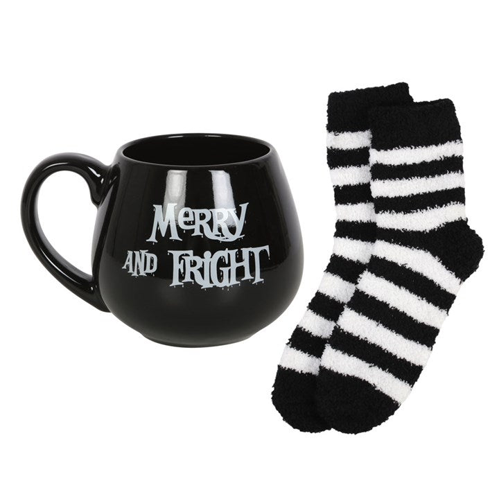 A black ceramic mug with 'Merry and Fright' text with a pair of black and white striped socks beside it.
