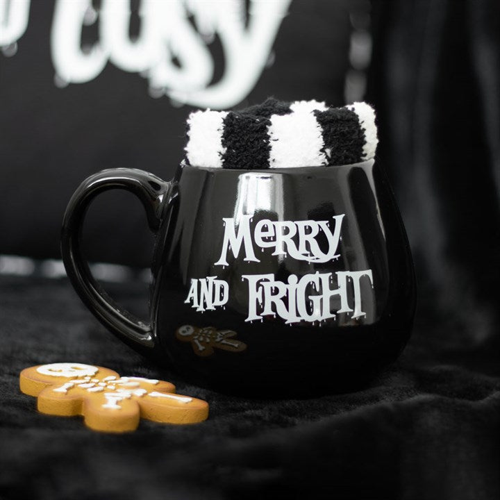 A black ceramic mug with 'Merry and Fright' text, placed on a black textured surface, with a pair of black and white striped socks inside it