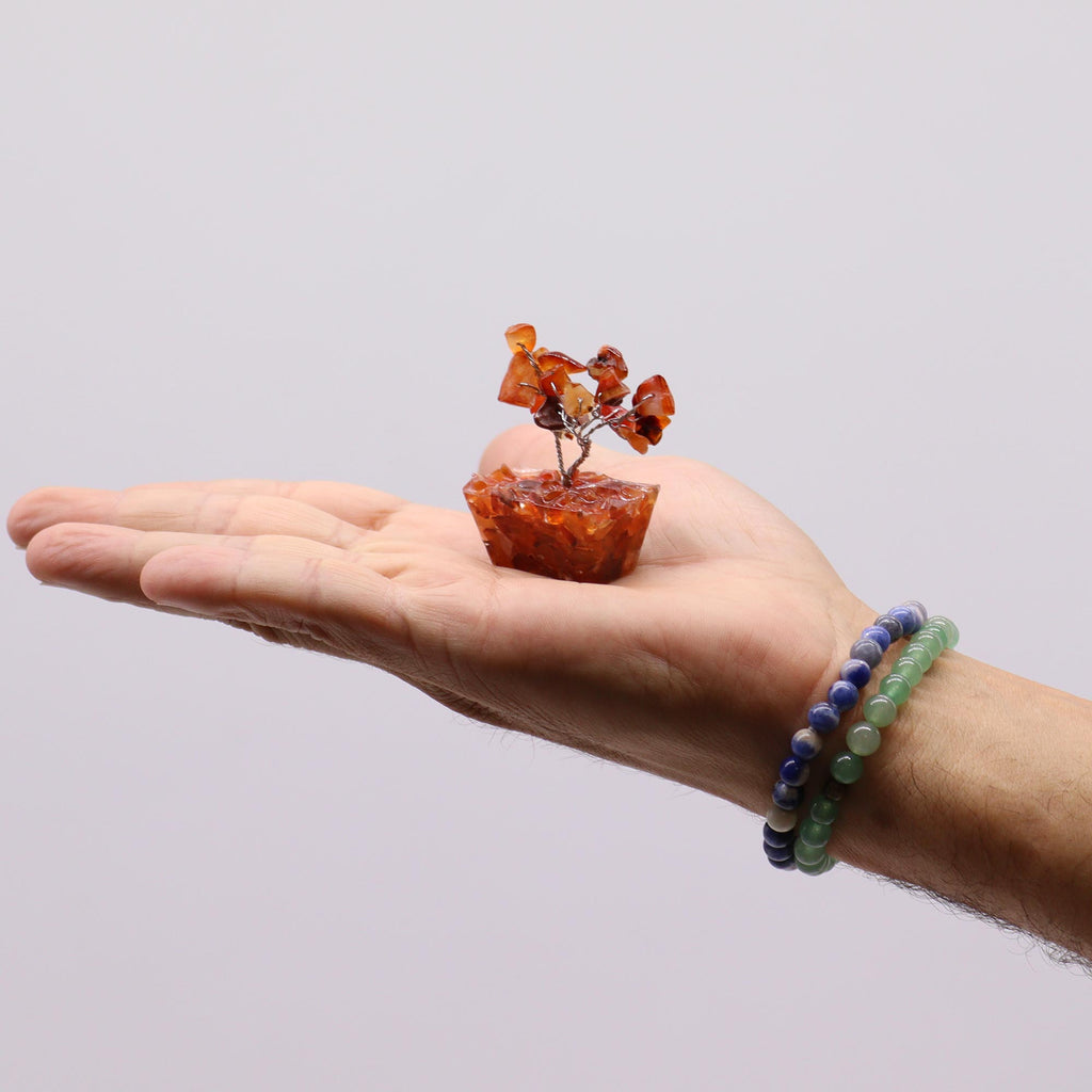 A mini carnelian tree on an orgonite base held in an open hand