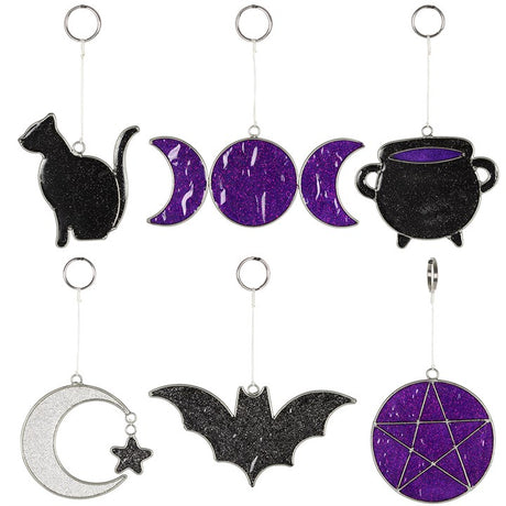 A selection of suncatchers in black, purple and silver designs. Designs include a cat, a cauldron, a crescent moon, a bat, a pentagram and a triple moon.