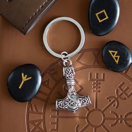 Silver Thor's hammer keychain on a brown surface with stones featuring rune symbols