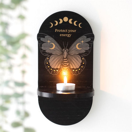 A black wooden altar shelf with a moth design and text 'PROTECT YOUR ENERGY' on it, with a candle lit on the shelf.