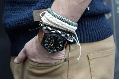 A person wearing a watch and a selection of bracelets with a combination of green and natural colour elements around it.