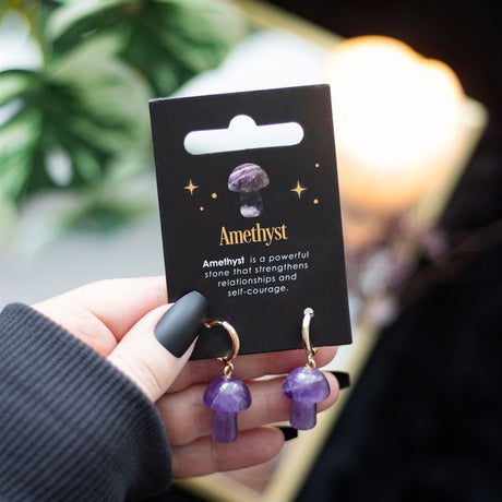 Mushroom shaped amethyst earrings on a black card being held in a hand