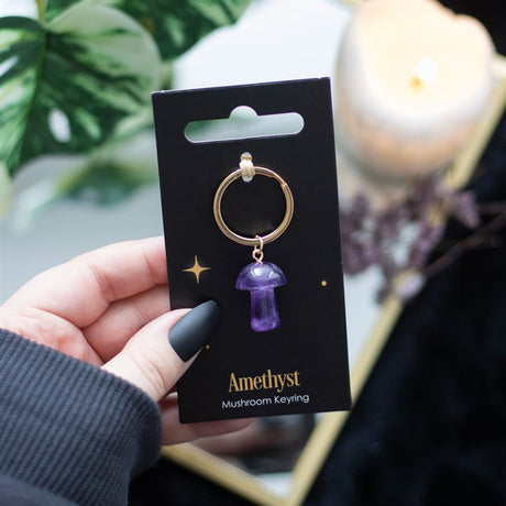 A mushroom shaped amethyst key ring on a black card being held in a hand