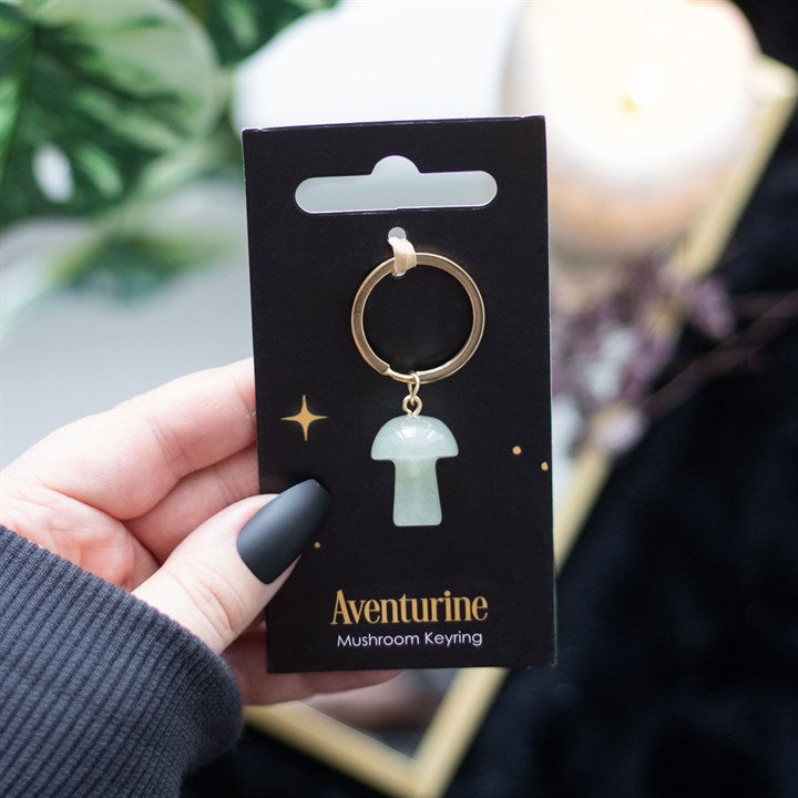 A mushroom shaped green aventurine key ring on a black card being held in a hand