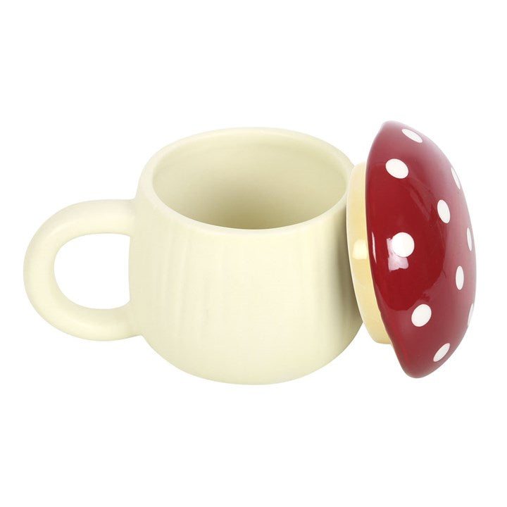 A white ceramic mug with a red mushroom-shaped lid which is on its side against a white background. 